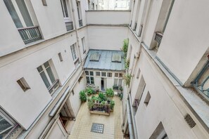 A narrow courtyard with multiple balconies, potted plants, and a tiled floor. - Charming Appartement 1ch/4p - Paris 17e (Paris)