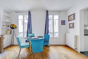 Ein Zimmer mit einem runden Glastisch, zwei blauen Stühlen, einer Dreibein-Stehlampe und einer Heizung.