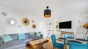 A modern living room with a grey sofa, blue chairs, a wooden coffee table, and a TV on a white wall. - Charming Appartement 1ch/4p - Paris 17e (Paris)