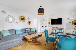 Ein modernes Wohnzimmer mit einem grauen Sofa, blauen Sesseln, einem Holztisch und einem Fernseher an einer weißen Wand.