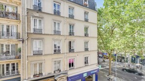 A multi-story building with balconies, storefronts, and a street view. - Charming Appartement 1ch/4p - Paris 17e (Paris)