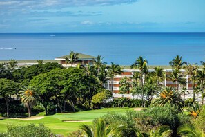 A golf course with a view of the ocean and a hotel with multiple floors and palm trees. - Wailea Ekolu 608 | Beautiful Wailea Condo with Ocean Views and Resort Amenities (Kihei)