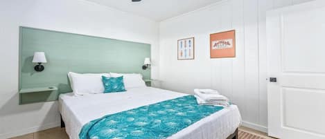 A hotel room with a bed, a ceiling fan, a nightstand, wall art, and a door.