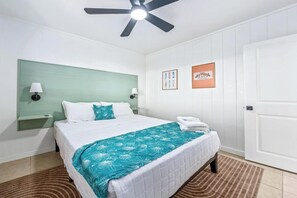 A hotel room with a bed, a ceiling fan, a nightstand, wall art, and a door. - New Listing, Kahaluu Surf Boutique, 2-bed, 2-bath (Kona)