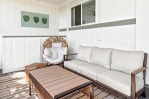A room with a sofa, a wicker chair, a wooden table, and a wall-mounted artwork. - New Listing, Kahaluu Surf Boutique, 2-bed, 2-bath (Kona)