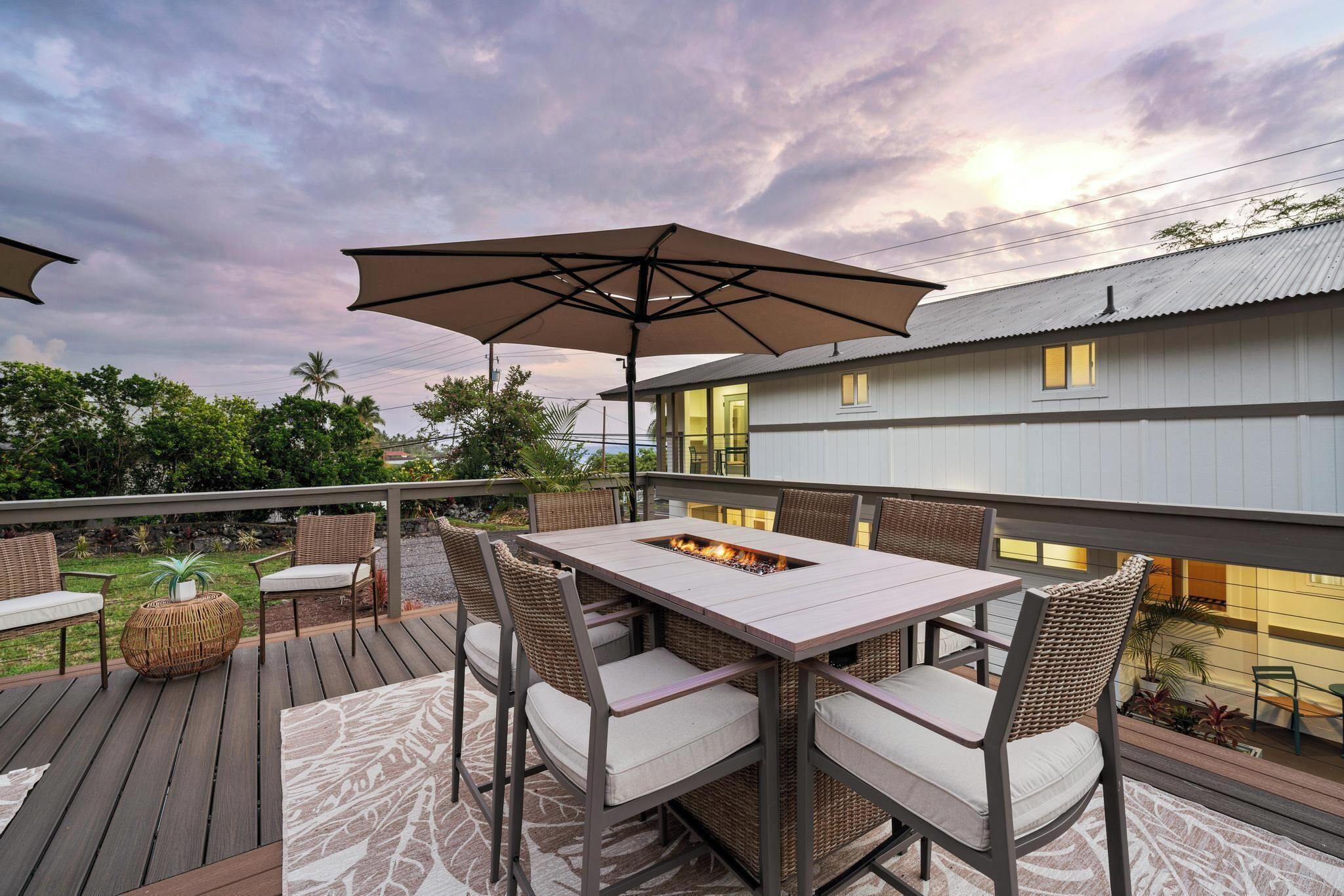 An outdoor deck with a fire pit table, wicker chairs, and a large umbrella.