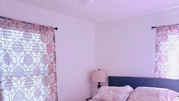 A bedroom with a bed, curtains, a ceiling fan, and a bedside lamp.