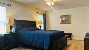 Quarto com cama, mesas de cabeceira, cômoda, ventilador de teto e janela com persianas.