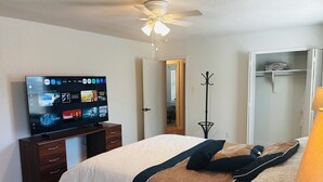 Quarto com uma cama, televisão sobre um suporte, cabideiro e guarda-roupa.