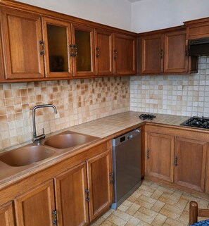 A kitchen with wooden cabinets, a stainless steel dishwasher, and a tiled backsplash. - Charming family home in the heart of Auvergne (Auzon)