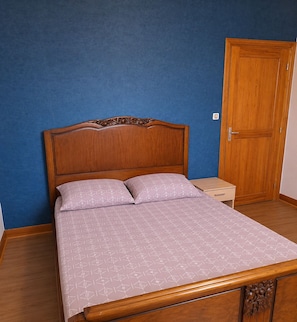 A single bed with a wooden headboard, two pillows, and a nightstand with a lamp. A wooden wardrobe is visible in the background. - Charming family home in the heart of Auvergne (Auzon)
