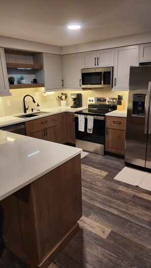 A modern kitchen with stainless steel appliances, wooden cabinets, and a central island. - Fully Remodeled 2Bed 2Bath Downtown Condo 3 Blocks From Lake Walk to Everything (McCall)