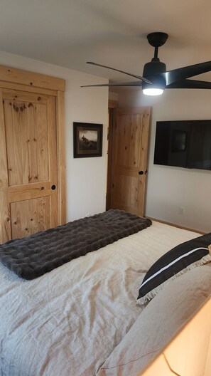 A bedroom with a bed, a ceiling fan, wooden doors, and a mounted television. - Fully Remodeled 2Bed 2Bath Downtown Condo 3 Blocks From Lake Walk to Everything (McCall)