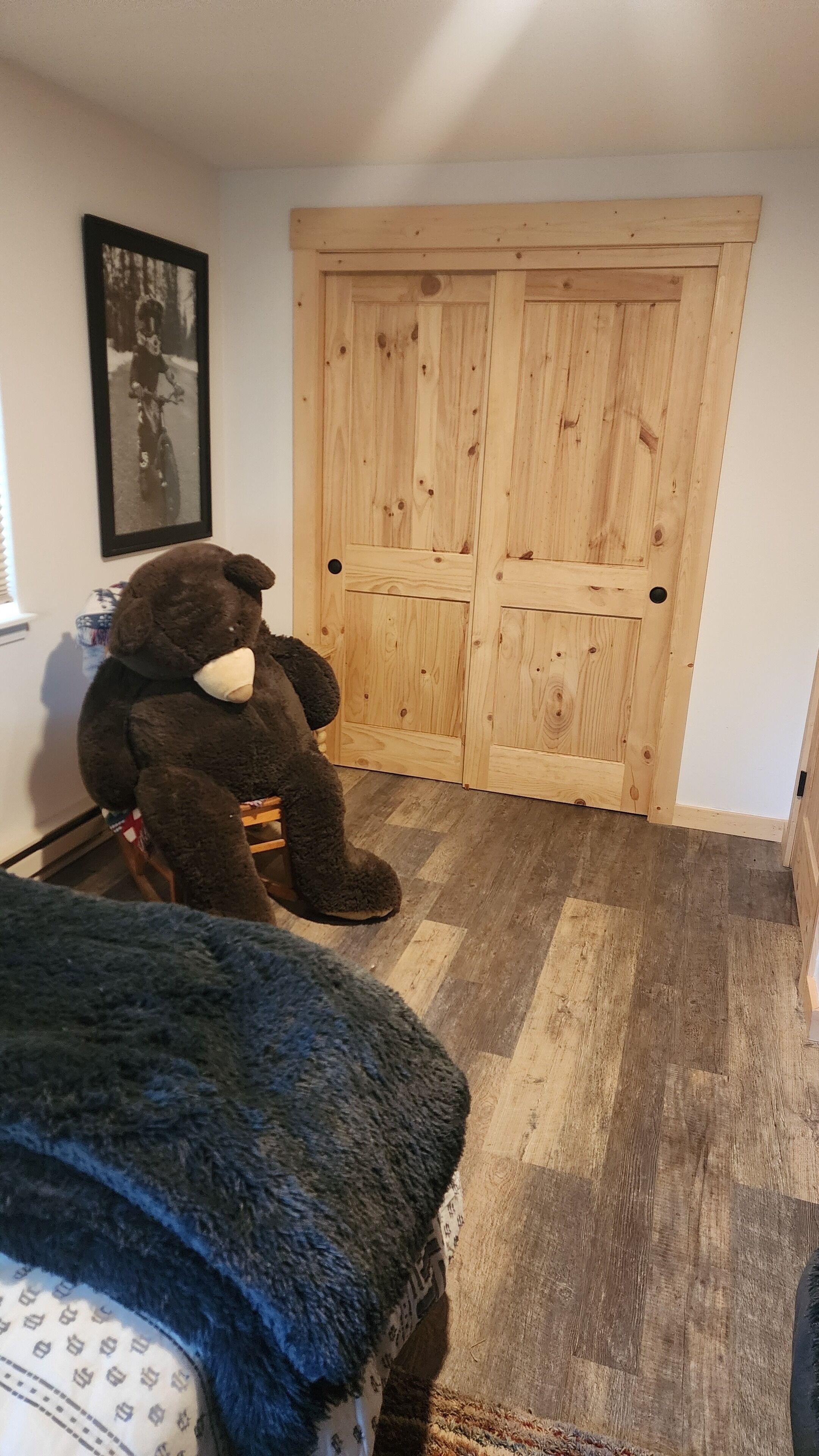 Una habitación con un armario de madera, un osito de peluche en una silla y un cuadro en la pared.