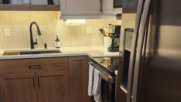 Eine moderne Küche mit einem Edelstahl-Kühlschrank, Holzschränken, einem eingebauten Backofen und einer Arbeitsplatte mit einer Kaffeemaschine.