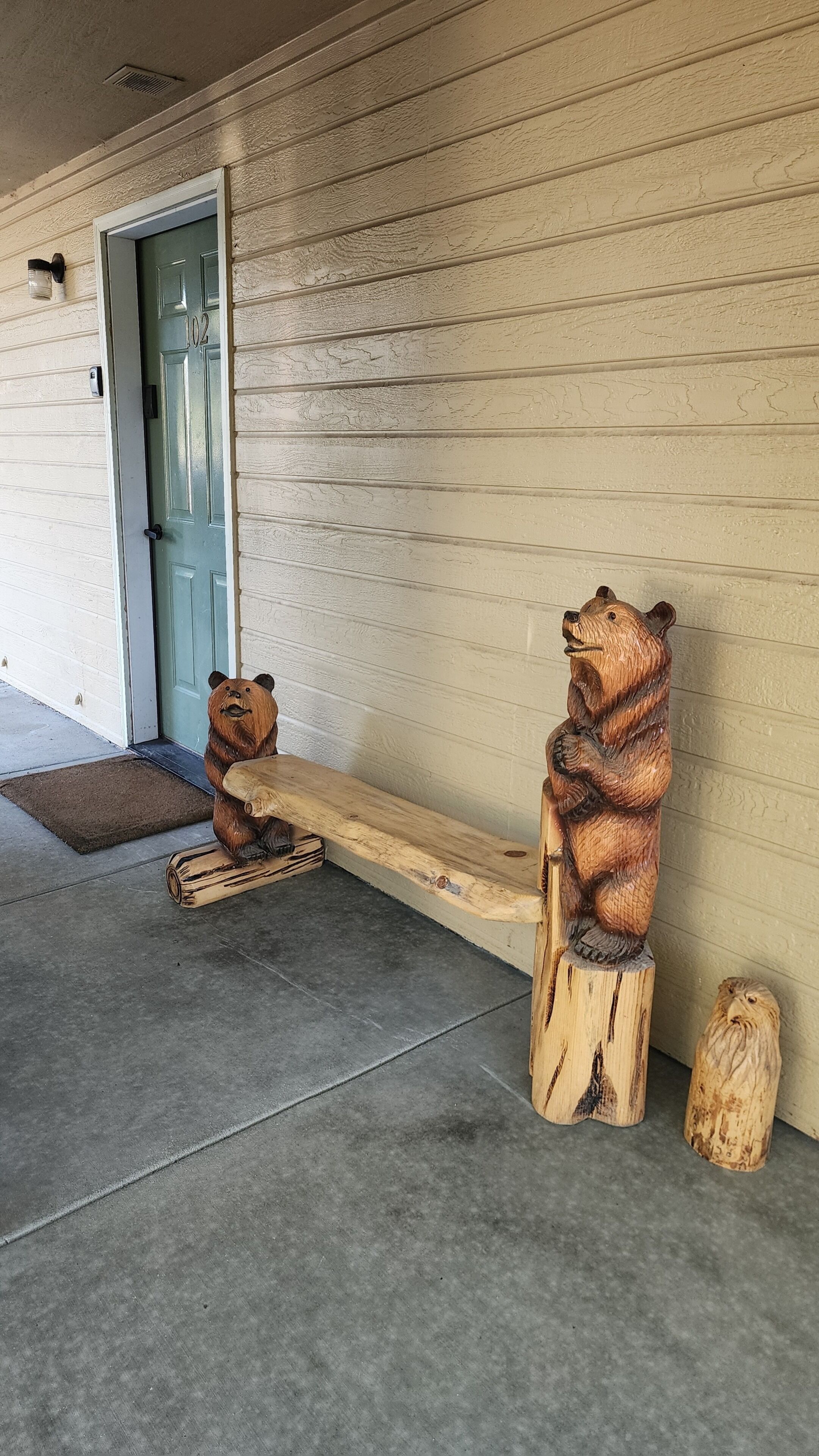 A wooden bench with bear carvings, a door with the number 102, and a concrete floor.