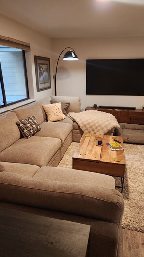A living room with a sofa, a coffee table, a lamp, a TV, and a window. - Fully Remodeled 2Bed 2Bath Downtown Condo 3 Blocks From Lake Walk to Everything (McCall)