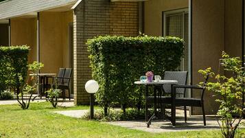 A hotel room with a brick exterior, a small garden area with a table and chairs, and a hedge.