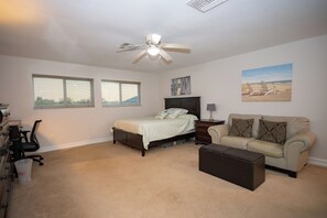 Um quarto com cama, escrivaninha, cadeira, sofá e um quadro na parede.