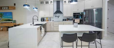 A modern kitchen with white cabinetry, a large island, and bar stools.