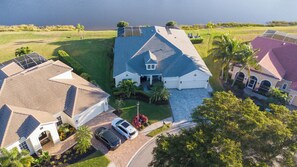 A residential area with houses, a driveway, and a body of water in the background. - The Ultimate Waterfront Retreat | 5BR • Pool & Spa • Resort Amenities (Cape Coral)