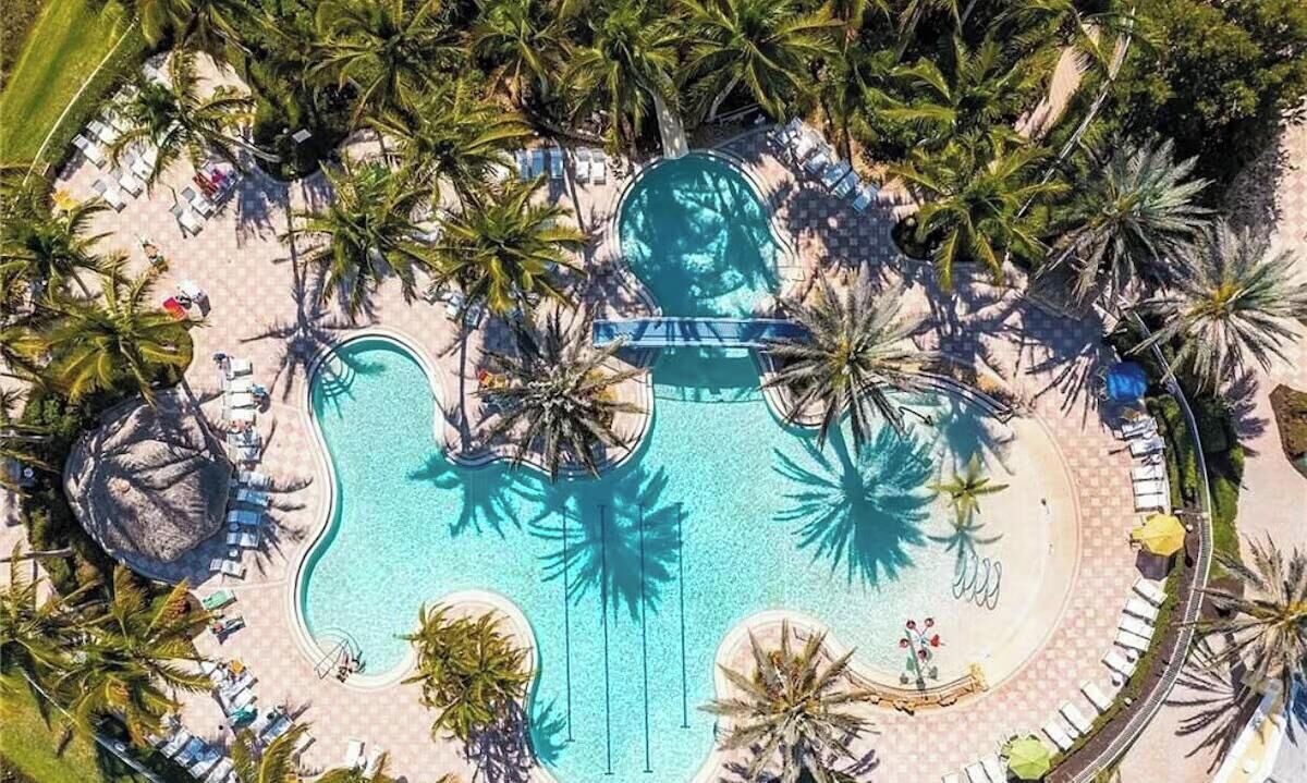 Vue aérienne d’un complexe hôtelier doté d’une piscine centrale, entourée de palmiers et d’espaces de détente.