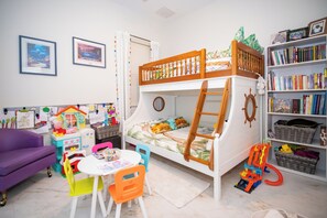 Quarto infantil com beliches, um espaço para brincar e uma estante de livros.