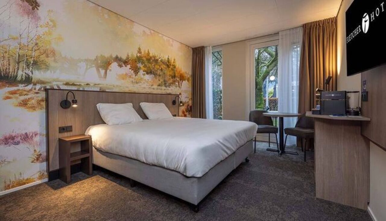 A hotel room with a bed, a desk, and a TV.