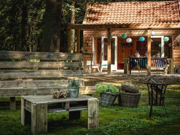 A rustic wooden building with a tiled roof, a covered outdoor seating area, and a bench in the foreground.
