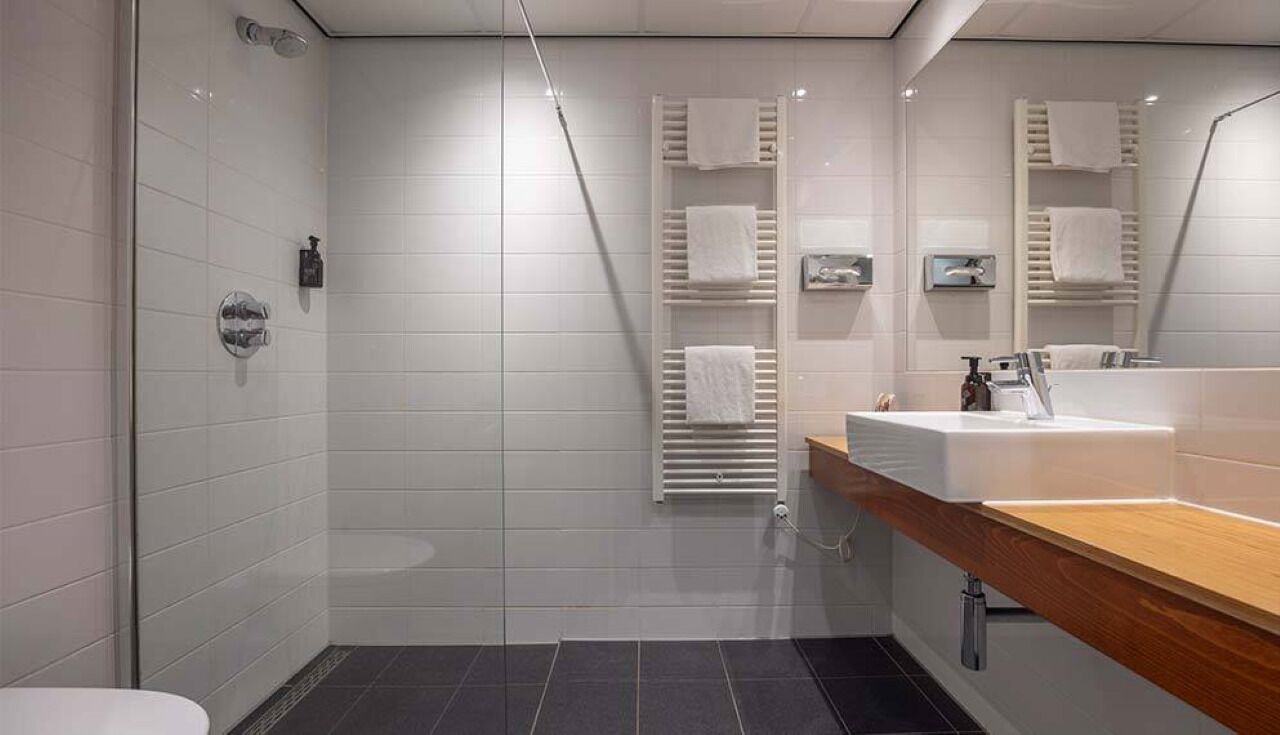 Une salle de bain moderne avec une douche à parois de verre, des murs recouverts de carreaux blancs, un meuble-lavabo en bois et un porte-serviettes intégré.