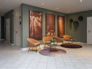 A modern lobby with three large wall-mounted deer paintings, a seating area with three chairs and a round table, and a tiled floor.
