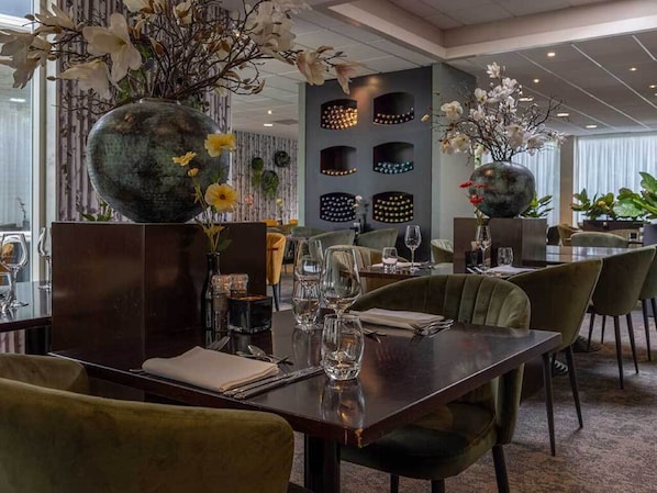 Een restaurant met een donker houten eettafel, omringd door groene bekleden stoelen.