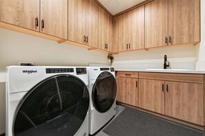 Ein Waschbereich mit zwei Whirlpool Waschmaschinen, Holzschränken und einer weißen Arbeitsplatte mit Waschbecken.