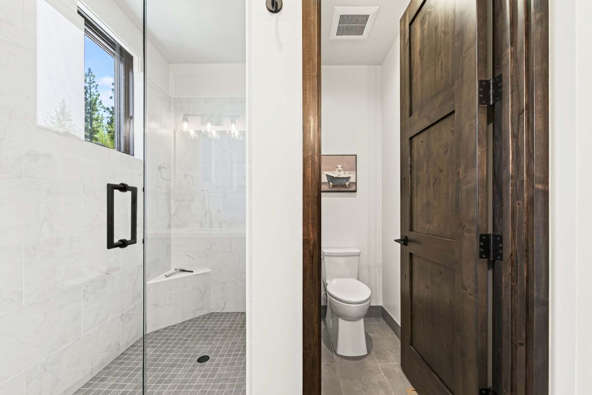 Un baño moderno con cabina de ducha de vidrio, un inodoro y una puerta de madera.