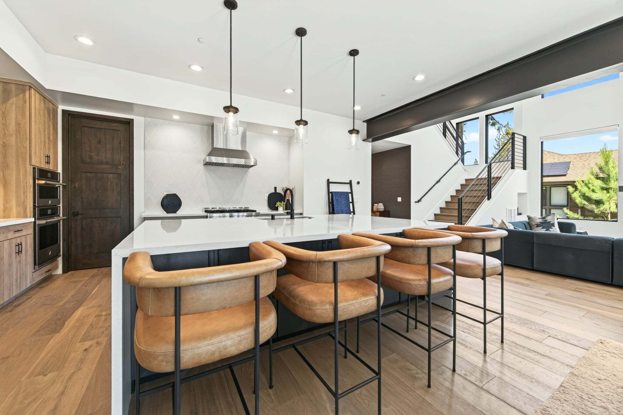 Una cocina moderna con una isla central, taburetes de bar y una escalera que lleva a un nivel superior.