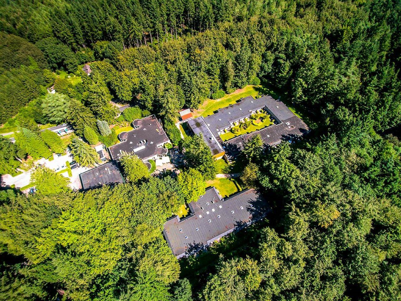 An aerial view of a residential area with multiple buildings surrounded by dense forest.