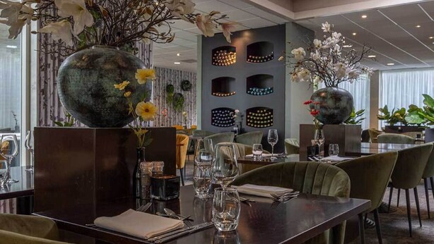 En restaurant med et mørkt træbord dækket til spisning, omgivet af grønne polstrede stole.