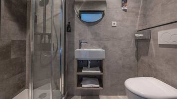 Een moderne badkamer met een glazen douchecabine, een wastafel met spiegel erboven en een toilet.