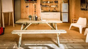 Et træinteriør med et picnicbord, hvide stole, et tekøkken og en hvidtavle.