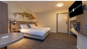 Una habitación de hotel con una cama, una mesa redonda, un cuadro en la pared y un televisor en la pared.