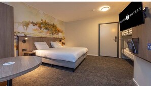 Een hotelkamer met een bed, een ronde tafel, een schilderij aan de muur en een televisie.