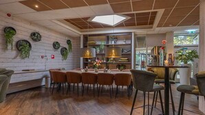 Un'elegante sala da pranzo con pavimento in legno, un tavolo lungo con sedie e un angolo bar con sgabelli.