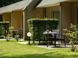 A hotel room with a brick exterior, a small garden area with a table and chairs, and a hedge.