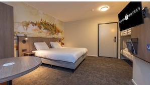 Una camera d'albergo con un letto, un tavolo rotondo, un quadro appeso e una televisione.