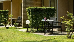 Une chambre d’hôtel avec une façade en briques, un petit jardin avec une table et des chaises, et une haie.