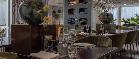Un restaurant avec une table en bois foncé, dressée pour le repas, entourée de chaises recouvertes d’un tissu vert.