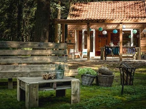 Un bâtiment rustique en bois, doté d’un toit en tuiles, d’un espace extérieur abrité avec des sièges et d’un banc au premier plan.