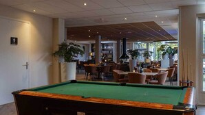 A pool table in a well-lit indoor space with a modern design, surrounded by comfortable seating and large windows allowing natural light. - 2 Serene Stays with Terrace Near Cycling Paths in Iconic Veluwe Trails (Putten)