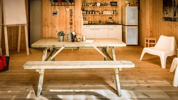 A wooden interior with a picnic table, white chairs, a kitchen area, and a whiteboard. - 2 Serene Stays with Terrace Near Cycling Paths in Iconic Veluwe Trails (Putten)