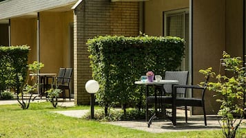 Una habitación de hotel con fachada de ladrillo, un pequeño jardín con mesa y sillas, y un seto.